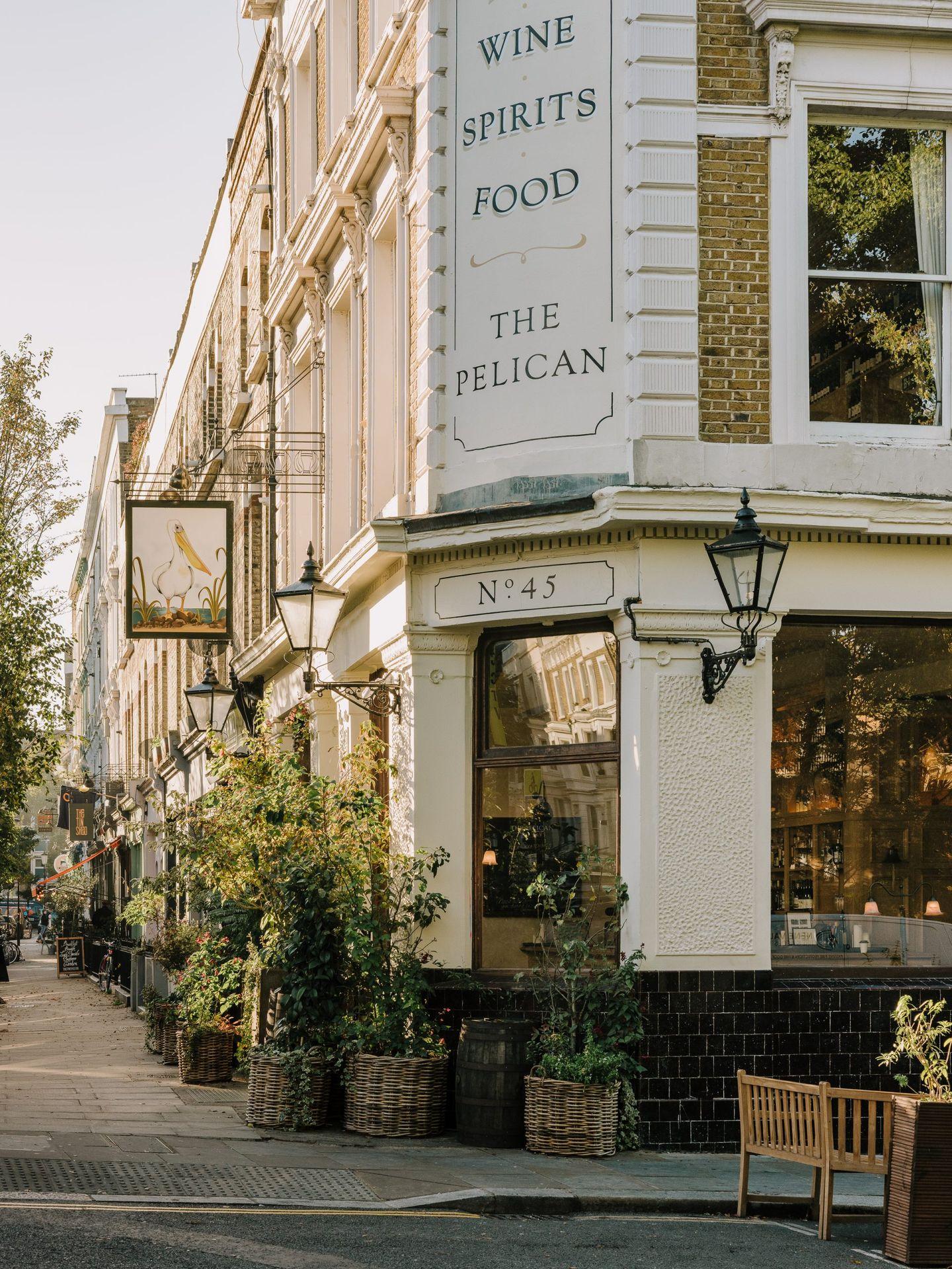 Exterior view of The Pelican pub with outdoor seating and greenery in a city street.